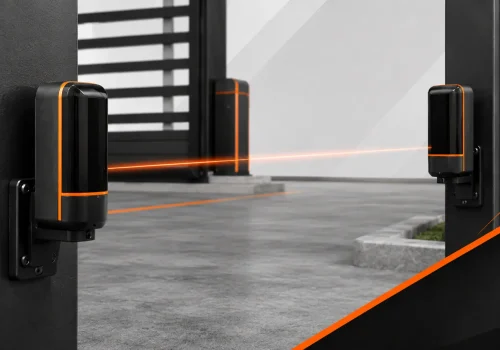 Infrared photocell sensors mounted on gate posts, projecting a safety beam across an automated driveway entrance.