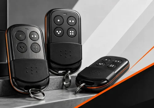 Automatic gate remote controls with black and orange casings, multi-button layouts, and key rings for access control.