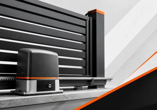 Automatic sliding gate motor beside a black metal fence, showing rack drive hardware for secure entry automation.